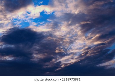 Dramatic Stormy Sky with Deep Blue and Golden Patches. A striking and atmospheric photograph of a powerful stormy sky.The image features a strong contrast between dark, heavy cumulus clouds and patches of vibrant, saturated blue sky and bright, sunlit white clouds. Sunlight highlights edges, creating beautiful golden hues within the dark grey cloud formation, adding dramatic depth. This photo is suitable as a backdrop for presentations, websites, digital banners, or book covers. It fits themes related to nature, weather forecasting, mood swings, environmental changes, or the force of nature.