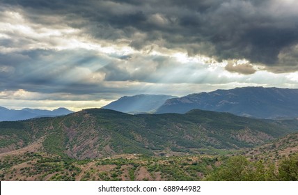 Dramatic stormy sky with sun rays through the clouds over a hilly valley with mountains in the distance