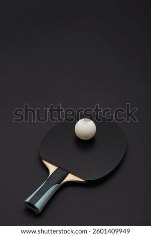 Dramatic studio photograph of a professional black ping pong paddle featuring sleek wooden handle with blue accents and competition-grade white ball, creating minimalist sports composition