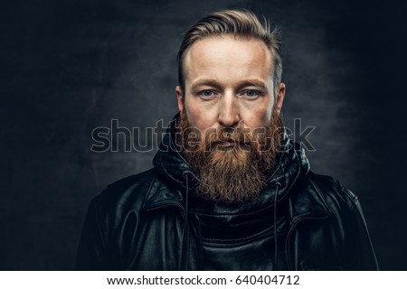 Dramatic studio portrait of redhead bearded male dressed in a leather jacket over dark grey vignette background.