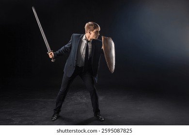 In a dramatic studio pose, a man in a navy suit stands poised with a sword and shield. The dark background emphasizes the contrast between corporate and medieval imagery.
