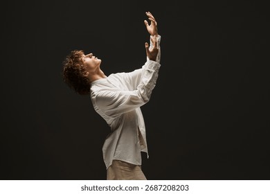 In a dramatic studio, a young man with curly hair passionately showcases his dance moves.