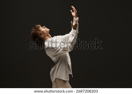 In a dramatic studio, a young man with curly hair passionately showcases his dance moves.