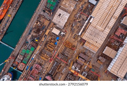 Dramatic stunning drone view of a vast coastal shipyard showcasing complex metal structures and massive cranes utilized for commercial vessel maintenance.
