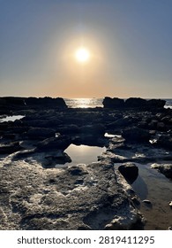 Dramatic sun over a rugged rocky coastline with reflections in calm tidal pools