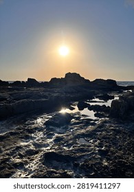 Dramatic sun over a rugged rocky coastline with reflections in calm tidal pools