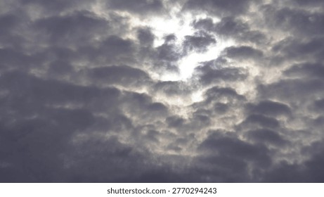 Dramatic sun peeking through heavy grey clouds in a moody sky