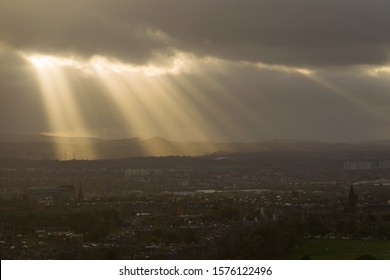 Dramatic sun ray through low clouds over city at sunset