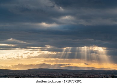 Dramatic sun ray through low clouds over city at sunset. The sun cuts through the clouds over the city. Sunbeams on the city