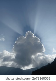 Dramatic sun rays behind dark cloud over mountain silhouette