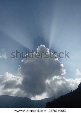 Dramatic sun rays behind dark cloud over mountain silhouette