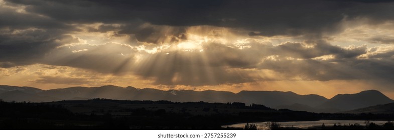 Dramatic sun rays breaking through clouds over mountain landscape in Liptov region, Slovakia. Golden sunset light illuminating silhouettes of Velka Fatra mountains.