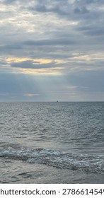Dramatic sun rays breaking through clouds over the Baltic Sea with a tiny distant boat on the horizon, vertical seascape.