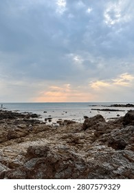 Dramatic sun rays breaking through clouds over a tropical rocky coastline at sunset, creating a peaceful seascape with natural copy space for travel, tourism, and nature themes.