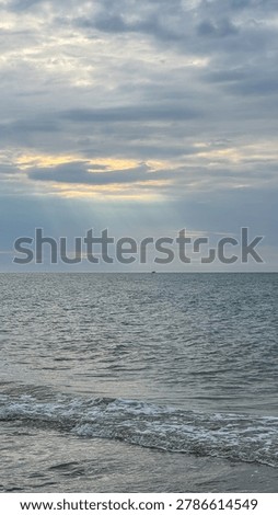 Dramatic sun rays breaking through clouds over the Baltic Sea with a tiny distant boat on the horizon, vertical seascape.