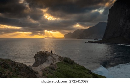 Dramatic sun rays at Miradouro do Guindaste with lonely runner, Madeira Island. Golden sunbeams break through heavy clouds over the Atlantic Ocean near Miradouro do Guindaste on Madeira Island, Portugal, while a solitary runner moves along a cliff edge in the foreground. Powerful seascape illustrating freedom, determination, adventure and dramatic coastal weather. - Powered by Shutterstock - Get 15% off with code: PIKWIZARD15