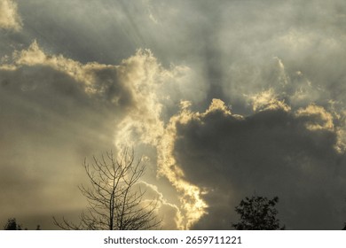 Dramatic sun rays pierce through dark and dramatic clouds creating celestial and awe-inspiring sky scene.