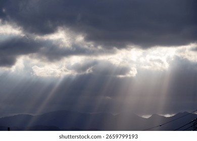 Dramatic sun rays pierce through dark clouds illuminating distant mountains and a serene sky.