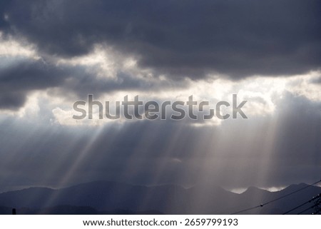 Dramatic sun rays pierce through dark clouds illuminating distant mountains and a serene sky.