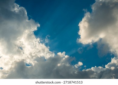 Dramatic Sun Rays Piercing Through Thick White Clouds in Blue Sky