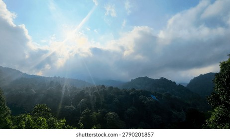 Dramatic Sun Rays Piercing Through Clouds Over Green Mountain Forest. Sunbeams Breaking Clouds in Blue Sky Above Mountain Ridge, Majestic Sunrise Wilderness Landscape Photography