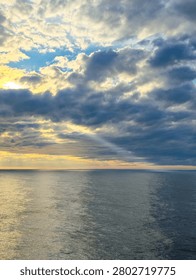 dramatic sunbeam breaks through dense storm clouds, illuminating a calm ocean with soft reflections. Atmospheric cloud formations and natural light create a striking seascape with an expansive horizon.