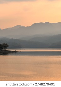 Dramatic sunbeams breaking through clouds over calm lake at sunset