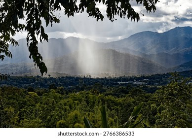 Dramatic sunbeams breaking through clouds over a lush green mountain valley and tropical forest.