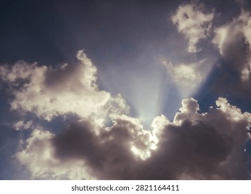 Dramatic sunbeams breaking through dark storm clouds in blue sky
Sun rays piercing through dense cumulus clouds against a deep blue sky, creating a dramatic crepuscular ray effect during daytime, captured from a low upward angle.