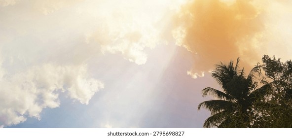 Dramatic sunlight breaking through thick clouds above tropical palm trees, creating radiant sun rays and a peaceful atmosphere. Natural sky landscape with beautiful cloud formations and warm lighting.