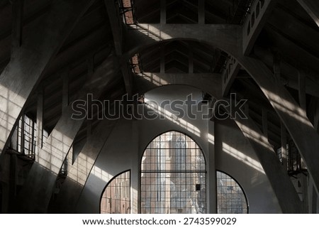 Dramatic sunlight creates diagonal shadow lines across concrete arches and arched windows inside large market hall. Wide architectural detail, strong symmetry, industrial modernist design, urban heritage public space.