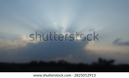 Dramatic sunlight rays pierce through dark storm clouds during a vibrant sunset, casting a silhouette over the horizon.