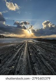 Dramatic sunrays breaking through clouds over flysch rock formations on the coast of Zumaia at sunset, Basque Country, Spain