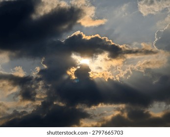 Dramatic sunrays pierce through heavy, dark storm clouds, casting golden light and shadows across a powerful sky. Majestic natural weather phenomenon.