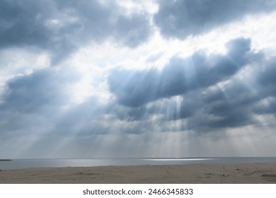 Dramatic sunrays piercing through the heavy cloud cover to illuminate the tranquil beach.