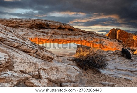 A dramatic sunrise casts a warm glow to the underside of Mesa Arch, Canyonlands National Park, Utah