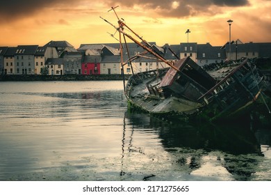 Dramatic sunrise cityscape scenery with old wooden sunken ship in Corrib river with colorful houses in the background at Claddagh, Galway City, Ireland 