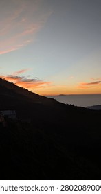 Dramatic sunrise sky with feather-like clouds over a dark mountain slope and rural road
