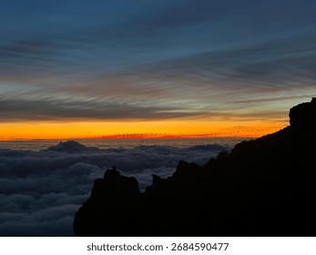 Dramatic sunset above the clouds with mountain silhouettes and vibrant sky, perfect for travel, adventure, wilderness, hiking, inspirational landscapes, natural beauty, and atmospheric scenic backgrou