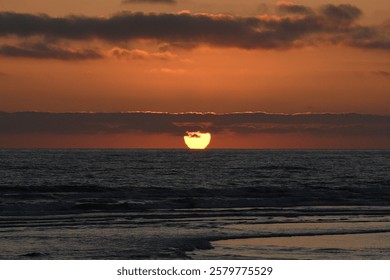 A dramatic sunset is captured in this image, with the sun setting over a tranquil ocean and wispy clouds suspended in the sky