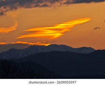 Dramatic sunset casting warm glow on snow capped mountain range