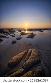 Dramatic sunset casting warm light on a rugged beach with boulders.
