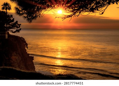 A dramatic sunset casts a warm golden glow over the Pacific Ocean, with waves gently rolling towards the shore