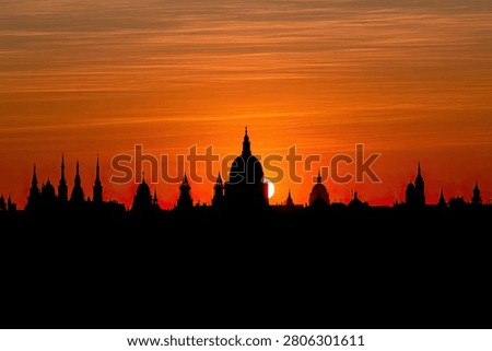 A dramatic sunset casts a warm orange glow over the iconic London skyline, silhouetting historic buildings including St Paul's Cathedral.