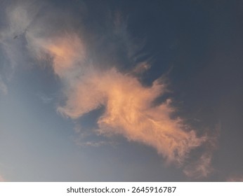 Dramatic sunset cloud formation with soft orange and pink hues against a deep blue sky, creating a dreamy and peaceful evening atmosphere.

