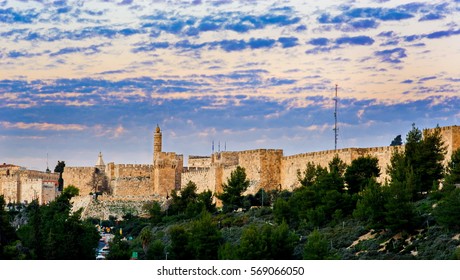 Dramatic sunset clouds over the Tower of David museum and the Jaffa Gate, with the Ottoman-built walls of Old City; stunning view from the green tree-covered Hinnom Valley or Gehenna, Jerusalem Israel