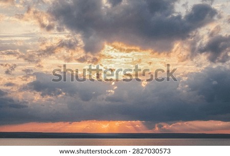 Dramatic sunset with golden crepuscular rays shining through dark clouds over water