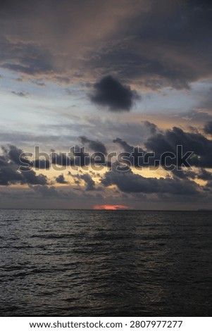 Dramatic Sunset Horizon with Last Sunbeams Peeking Through Dark Clouds over the Sea
