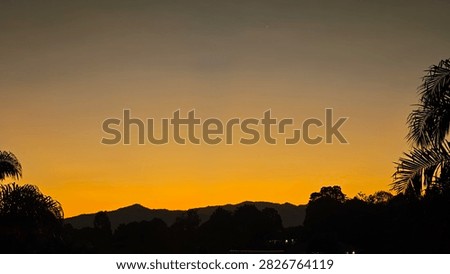A dramatic sunset illuminates clouds above rooftops and power lines. The bright golden light results from Rayleigh scattering, where longer wavelengths dominate near the horizon, creating vivid warm colors in late‑day skies.