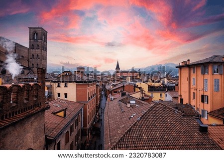 Dramatic sunset illuminates the medieval skyline of Bologna, Italy, casting warm light over the historic terracotta rooftops and the iconic leaning towers. This panoramic aerial view highlights the rich architectural heritage of the Emilia-Romagna capital. The vibrant evening cityscape showcases a premier European travel destination, renowned for its ancient university, classic Italian charm, and cultural history.
